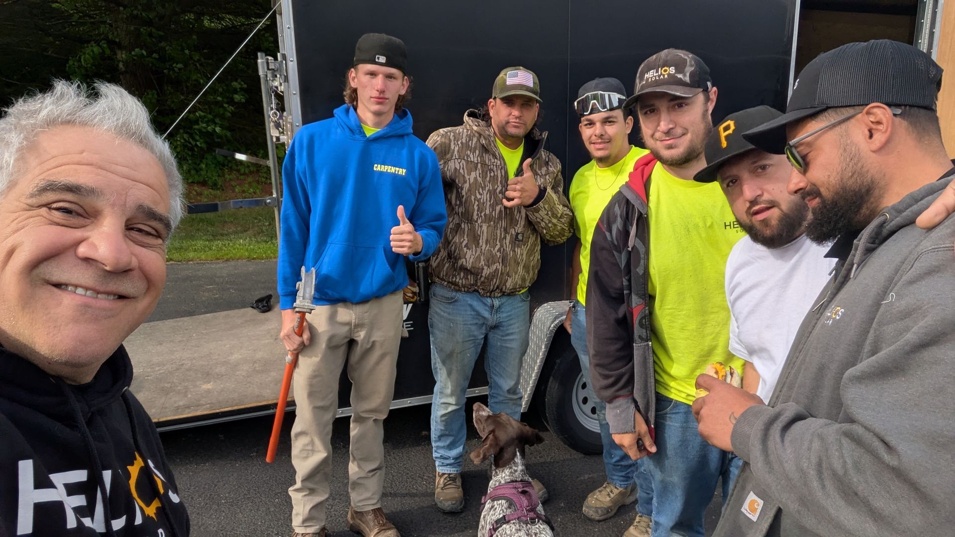 A group of men are posing for a picture with a dog in front of a trailer.