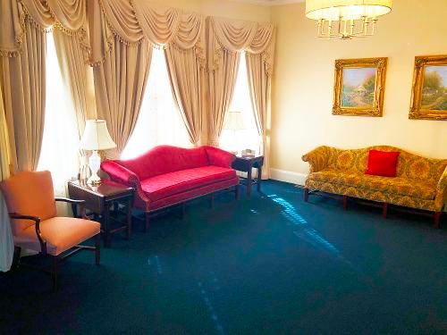 A living room with two couches , two chairs , a table , and two paintings on the wall.