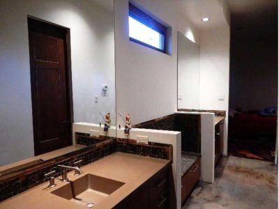 Bathroom with dark brown door, two sinks, mirrors, a small window, and concrete flooring.