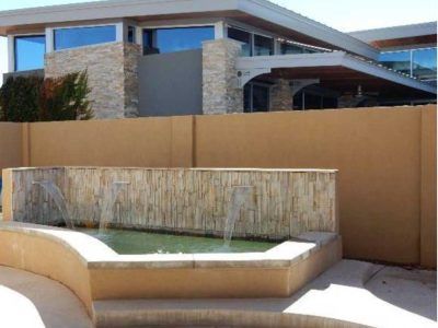 Fountain with water cascading over stone wall, beige walls, and modern building with reflective windows.