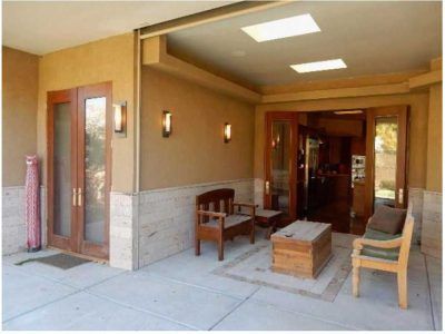 Covered patio with wooden furniture and double doors. Beige walls, skylights.