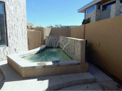 Small outdoor water feature with stone surround and flowing fountains, sunny day.