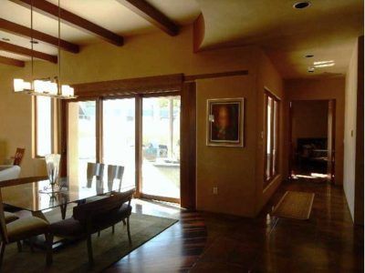 Dining room with glass table, chairs, and large sliding doors. Wooden beams and floors, painting on the wall.