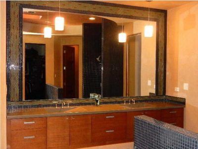 Bathroom with large mirror framed by mosaic tile, wooden vanity, and pendant lights.