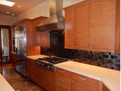 Modern kitchen with wooden cabinets, stainless steel appliances, and dark tile backsplash.