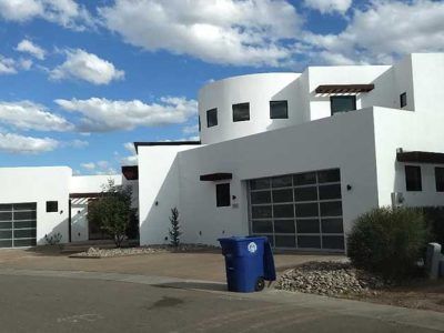 White modern home with a blue trash can on the curb; blue sky with white clouds.