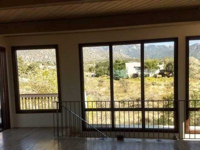 Interior view with large windows overlooking a landscape. Brown frames, balcony, and mountains in the distance.