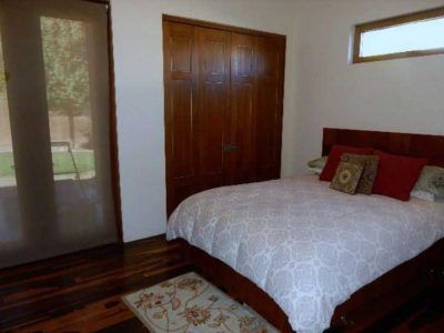 Bedroom with a wooden bed, patterned bedding, and a brown closet. Window with a shade.