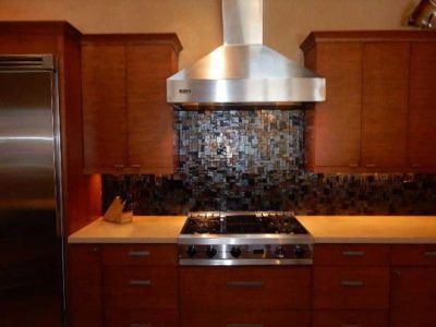 Kitchen with cherry wood cabinets, stainless steel range hood, and multi-colored mosaic backsplash.