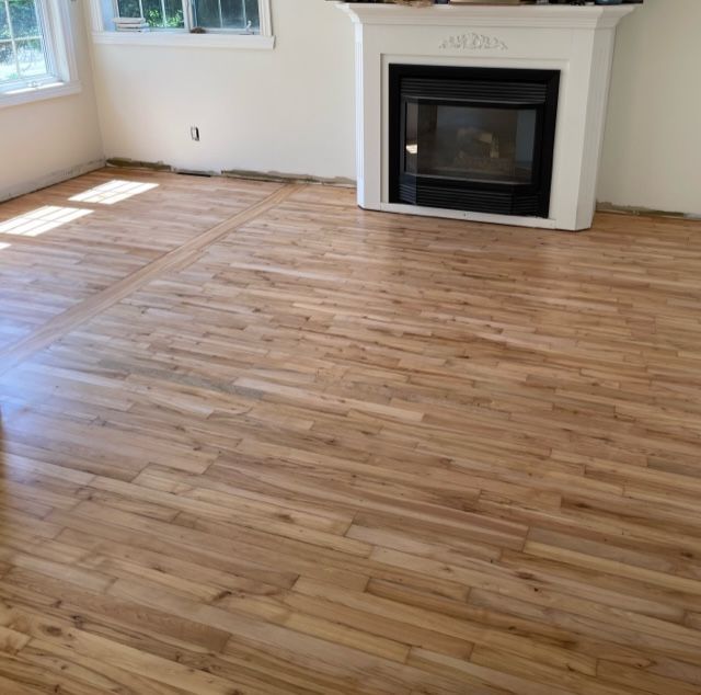 Plancher de bois clair dans une pièce avec cheminée blanche, fenêtres et murs blancs.