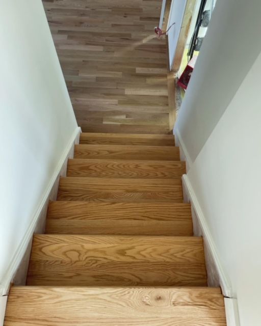 Escalier en bois menant à l'étage, bordé de murs blancs.