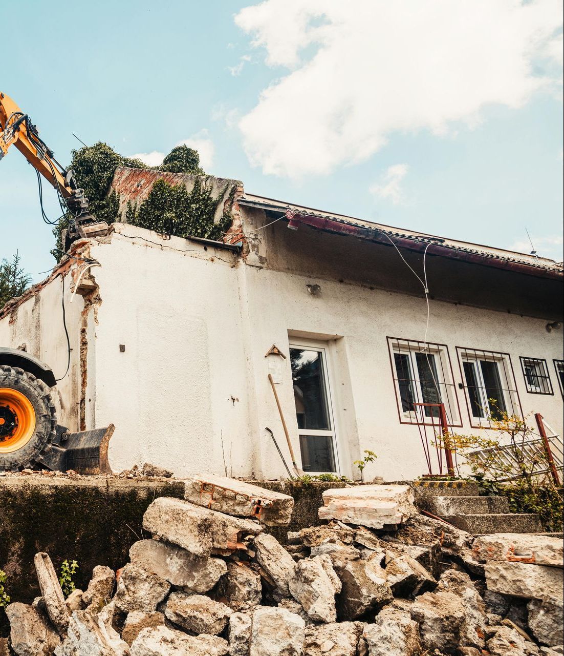 A bulldozer is demolishing a house with a pile of rocks in front of it.