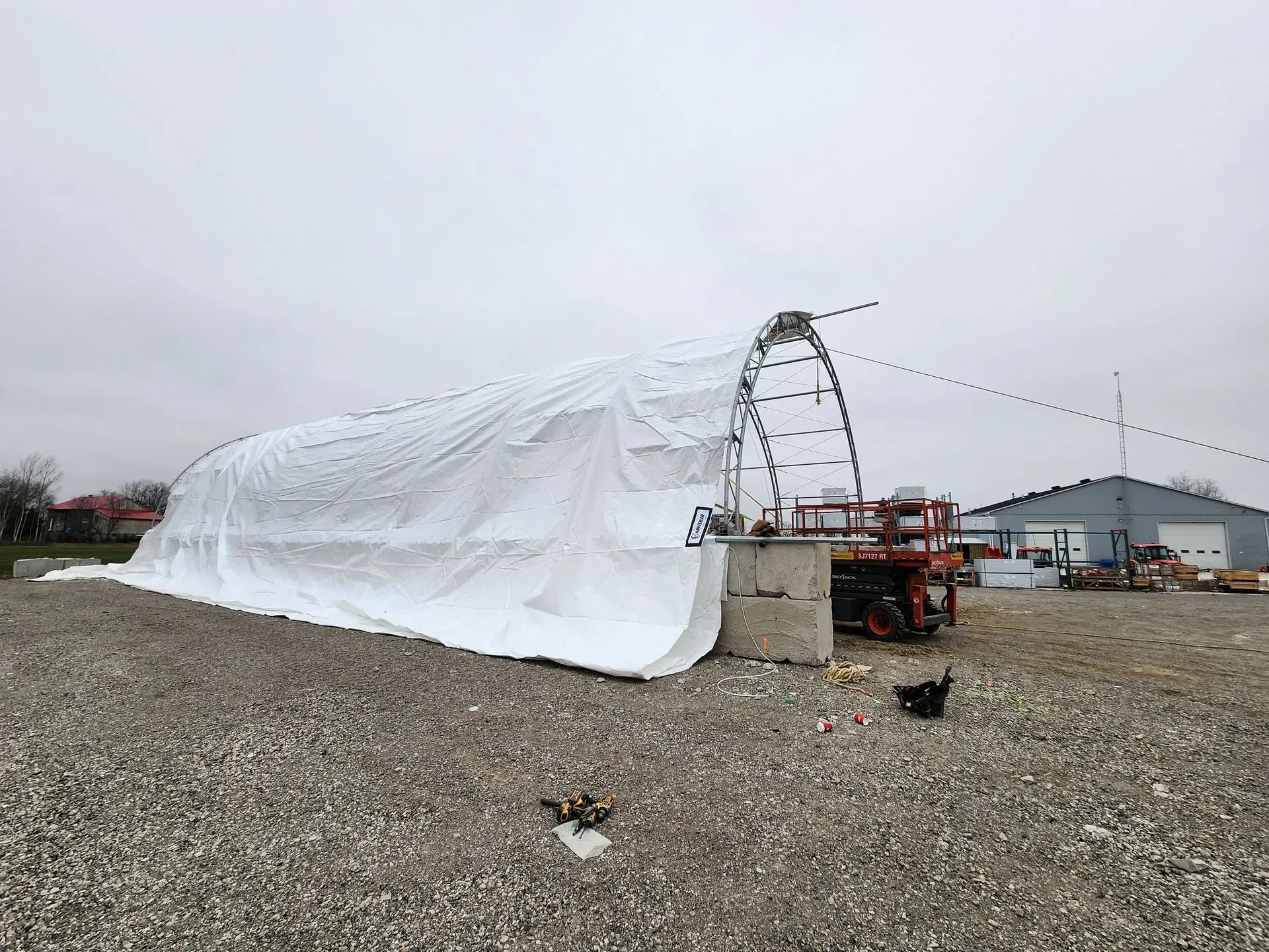 A large white tarp is covering a building in a gravel lot.