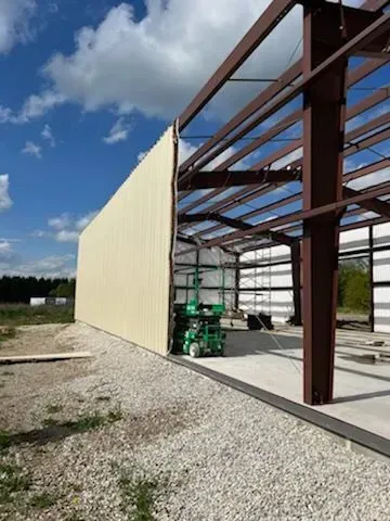 A large metal building is being built on a gravel lot.