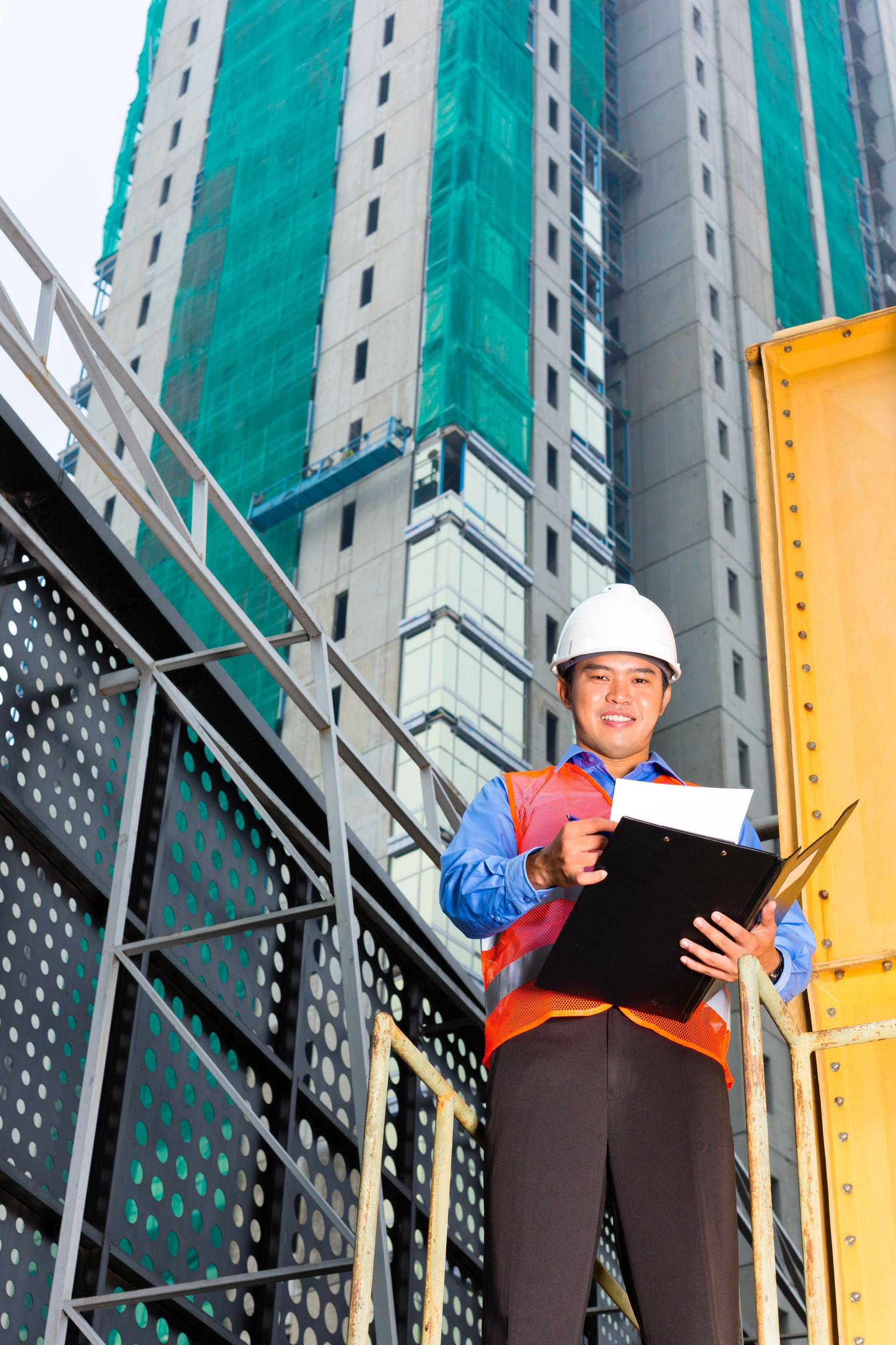 A construction worker is holding a clipboard in front of a tall building.