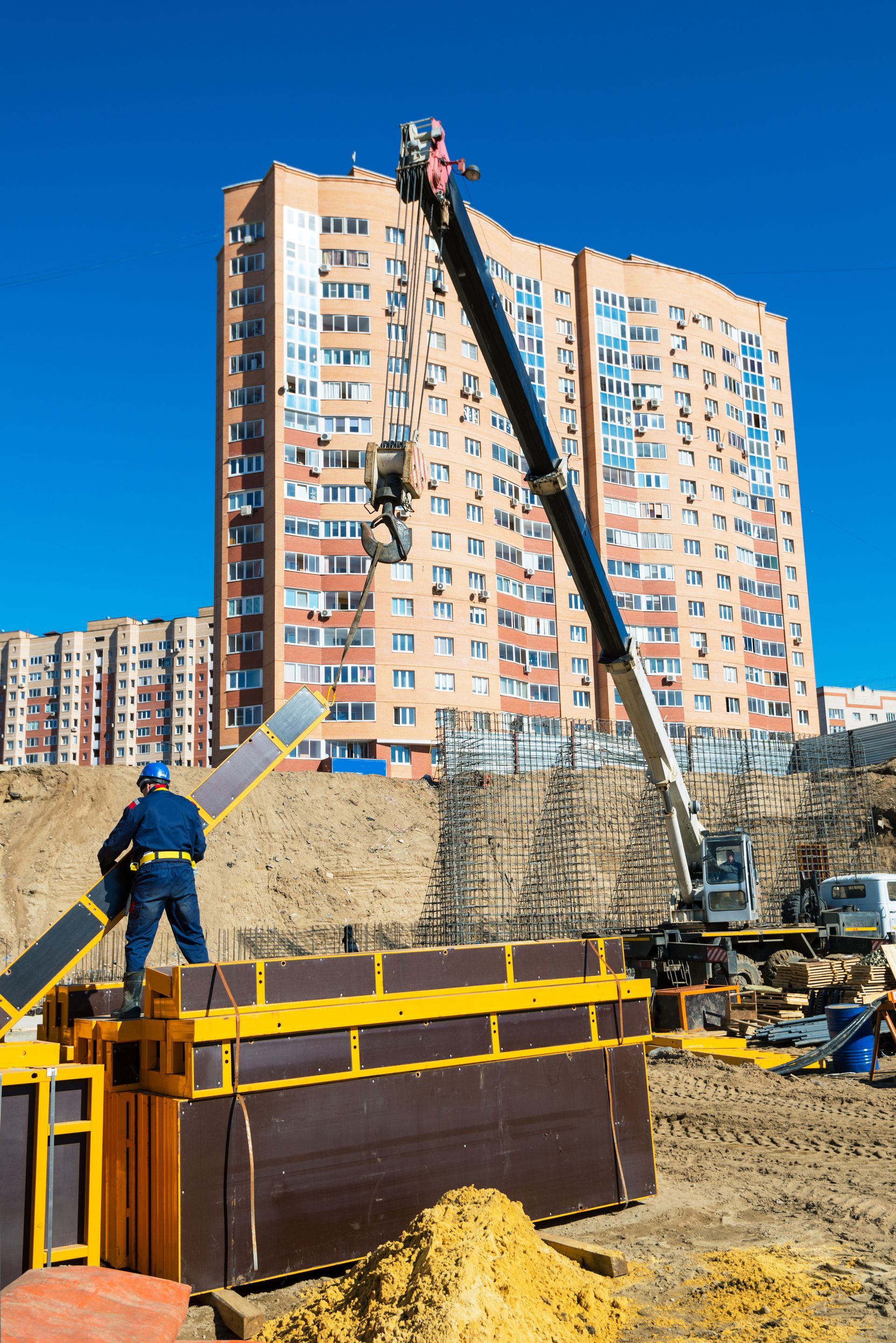 A construction site with a large building in the background and a crane in the foreground.