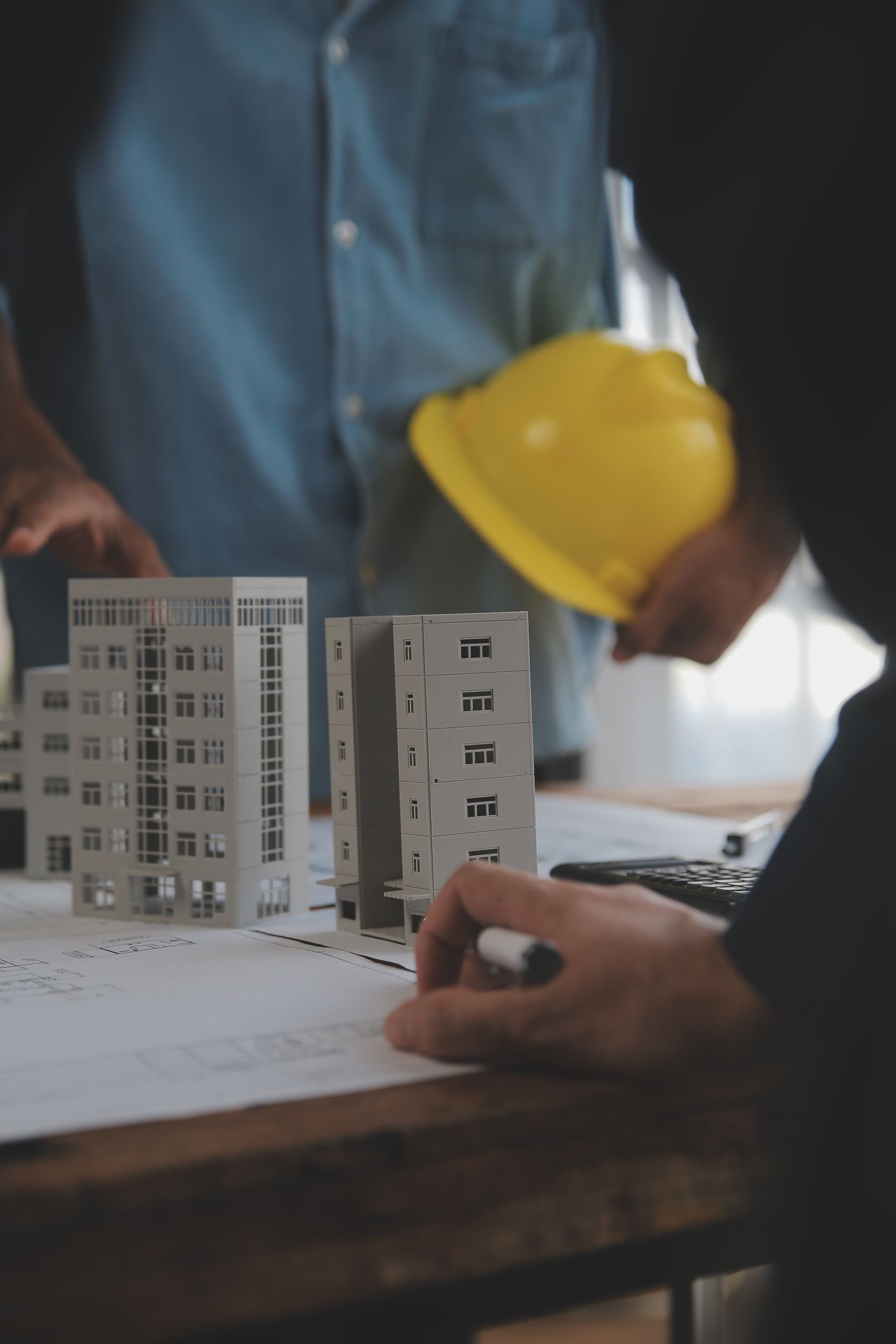A man wearing a yellow hard hat is looking at a model of a building.