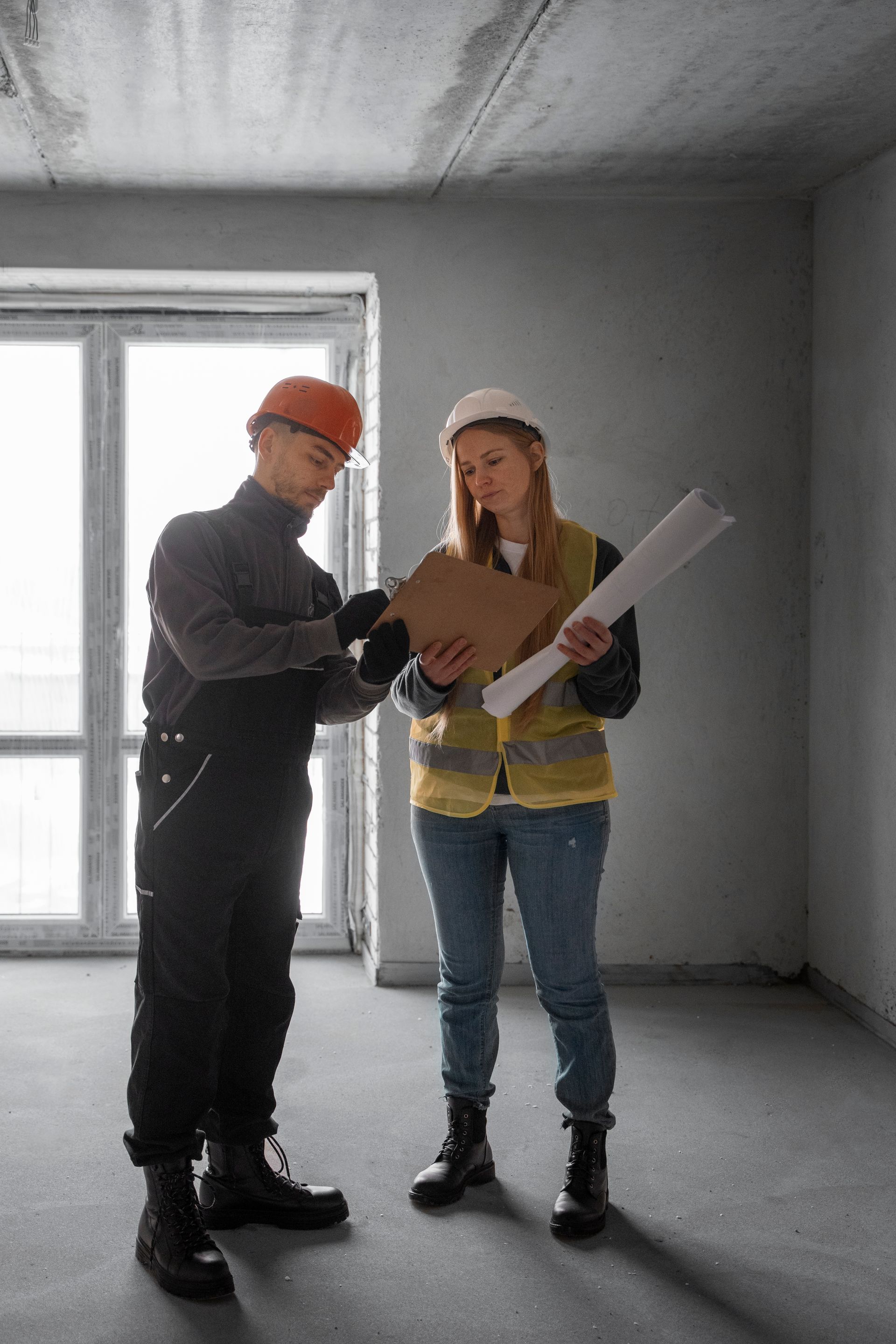 A man and a woman are standing in an empty room looking at a clipboard.