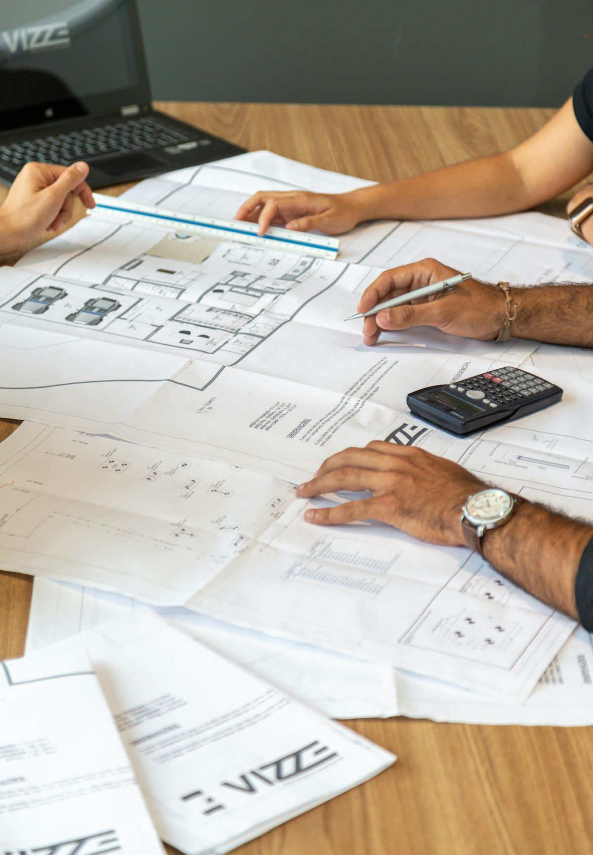 People reviewing floor plans and documents at a desk with calculator and pens