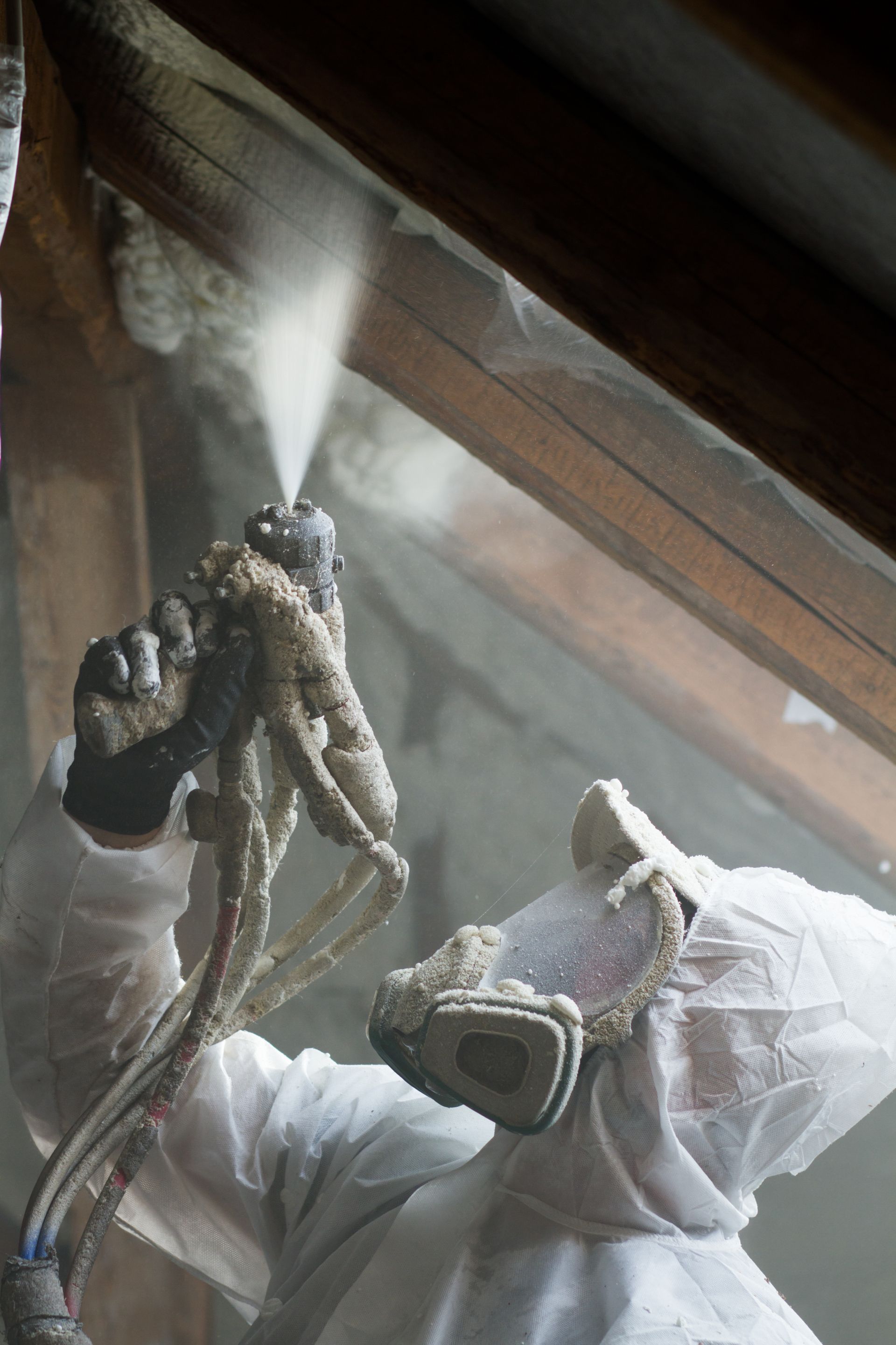 A man in a protective suit is spraying foam on a window.