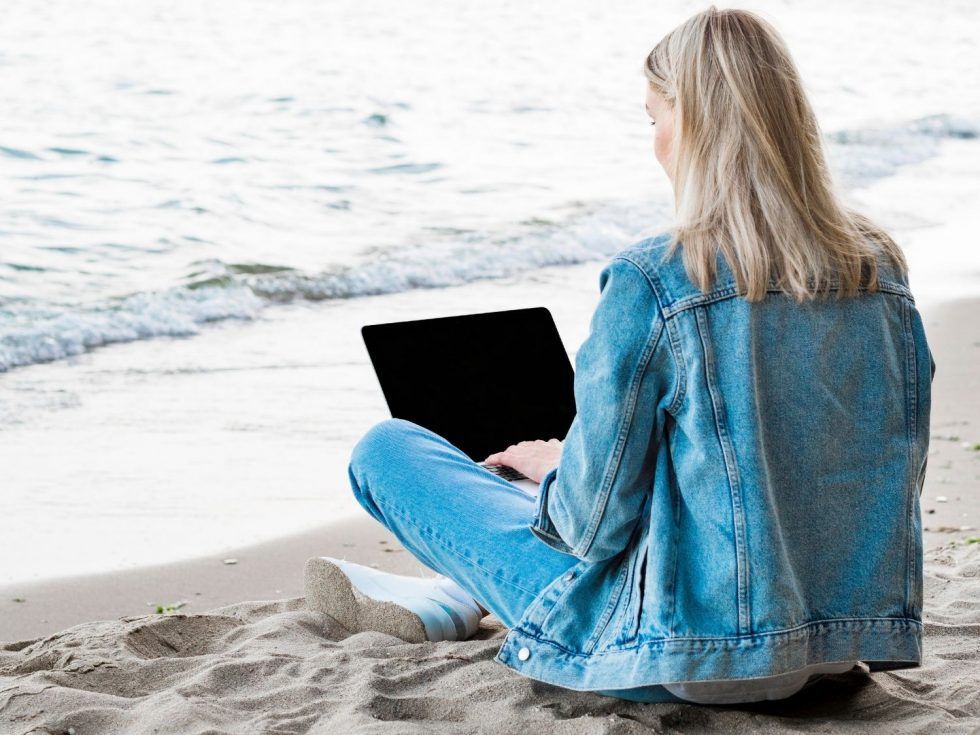 A woman is sitting on the beach using a laptop computer.