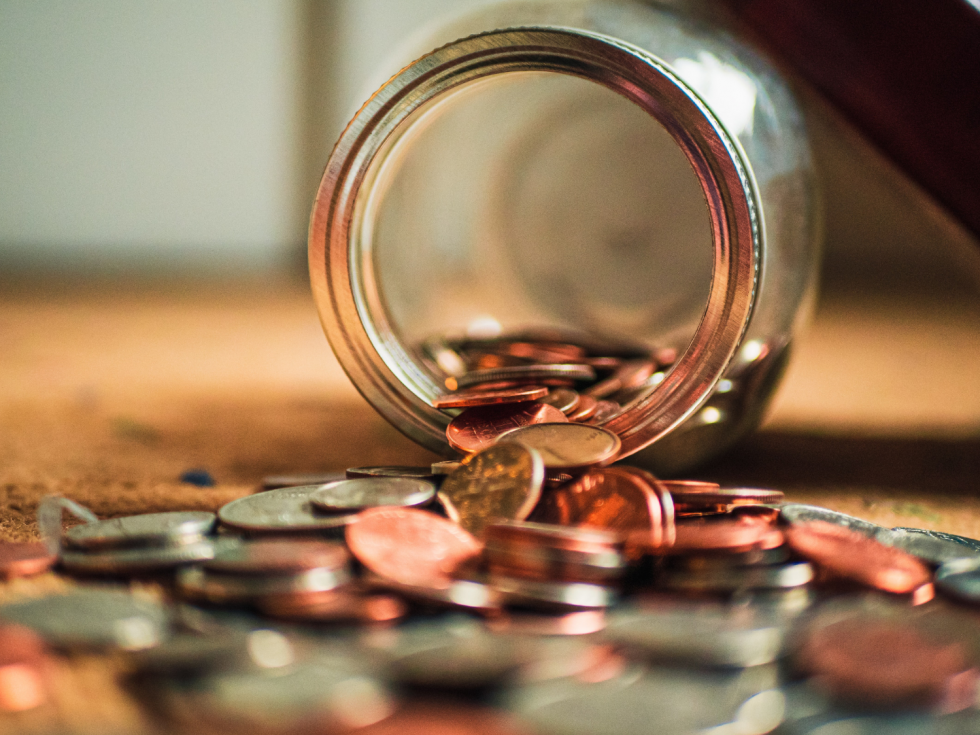 A jar filled with coins is spilling out onto a table.