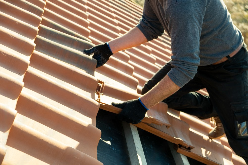 Worker hands skillfully insta vibrant yellow ceramic roofing tiles on wooden boards, showcasing precision and craftsmanship in the construction process.