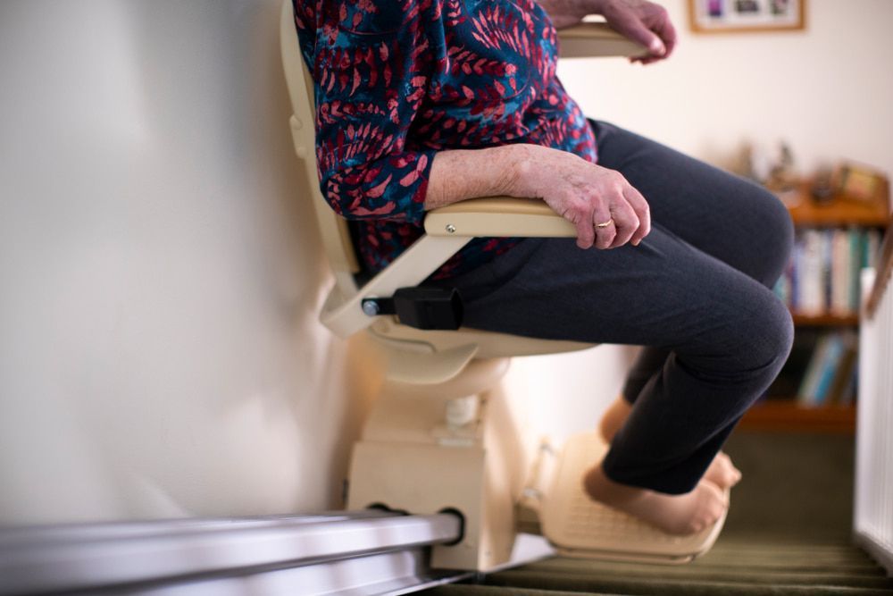An Elderly Woman Is Sitting On A Stair Lift — Master Lifts Cairns in Cassowary Coast, QLD
