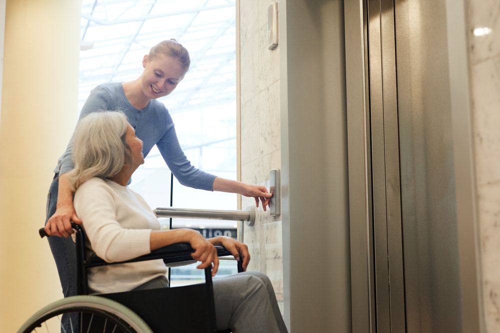 A Woman In A Wheelchair Is Being Helped Into An Elevator By A Nurse — Master Lifts Cairns in Cairns, QLD