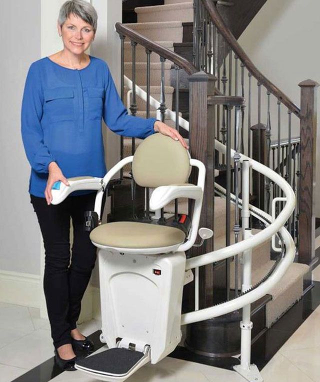 A Woman In A Blue Shirt Is Sitting On A Stair Lift — Master Lifts Cairns In Cairns, Qld