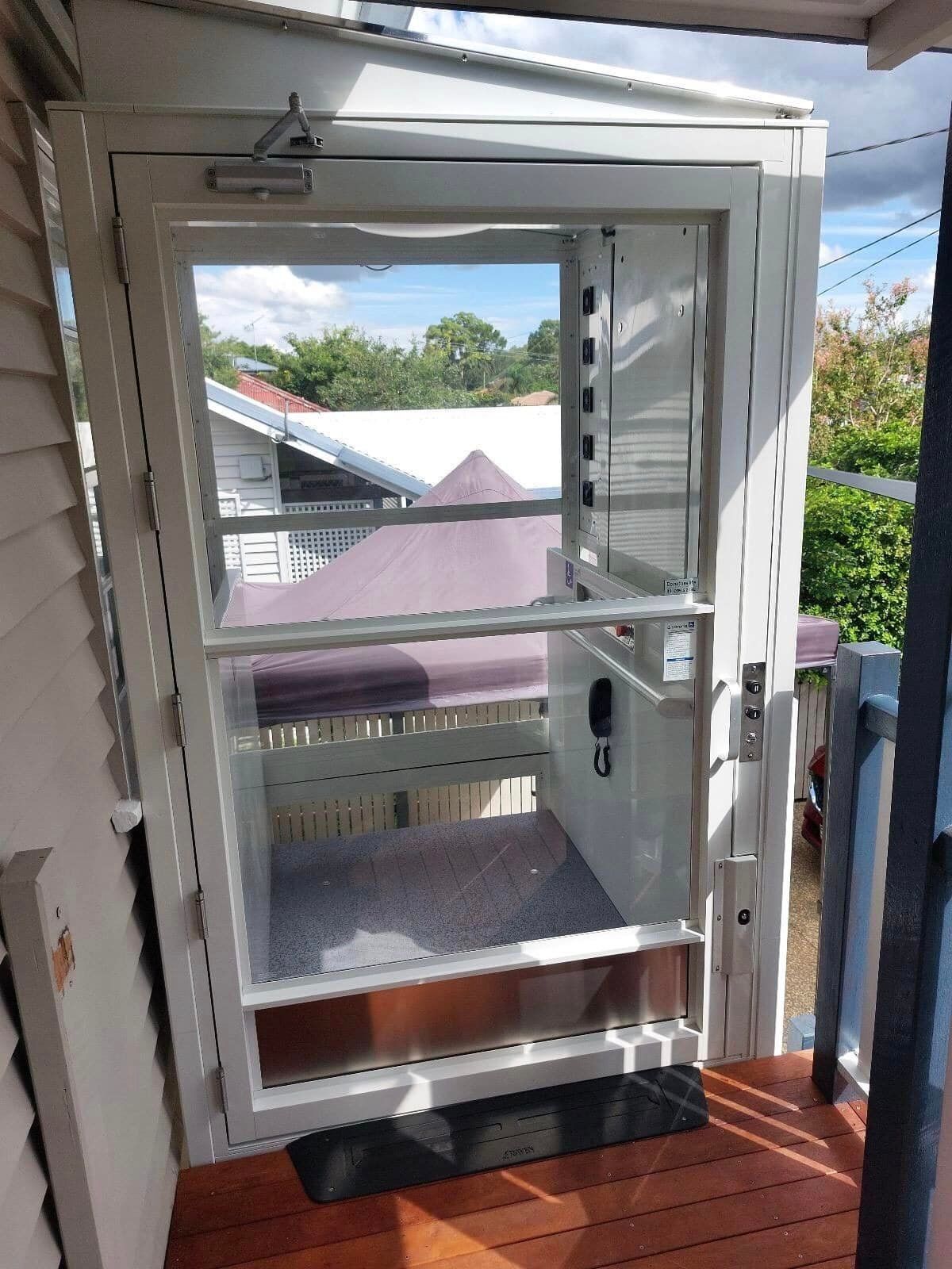A Small Elevator Is Sitting on Top of A Wooden Deck Next to A House — Master Lifts Cairns in Cairns, QLD