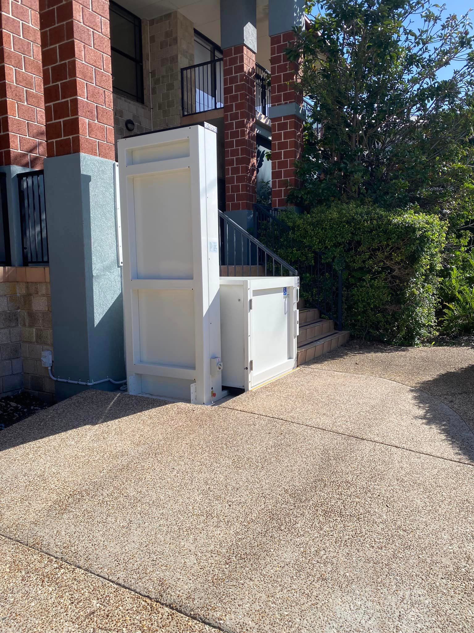 A White Lift Is Sitting in Front of A Brick Building — Master Lifts Cairns in Cairns, QLD
