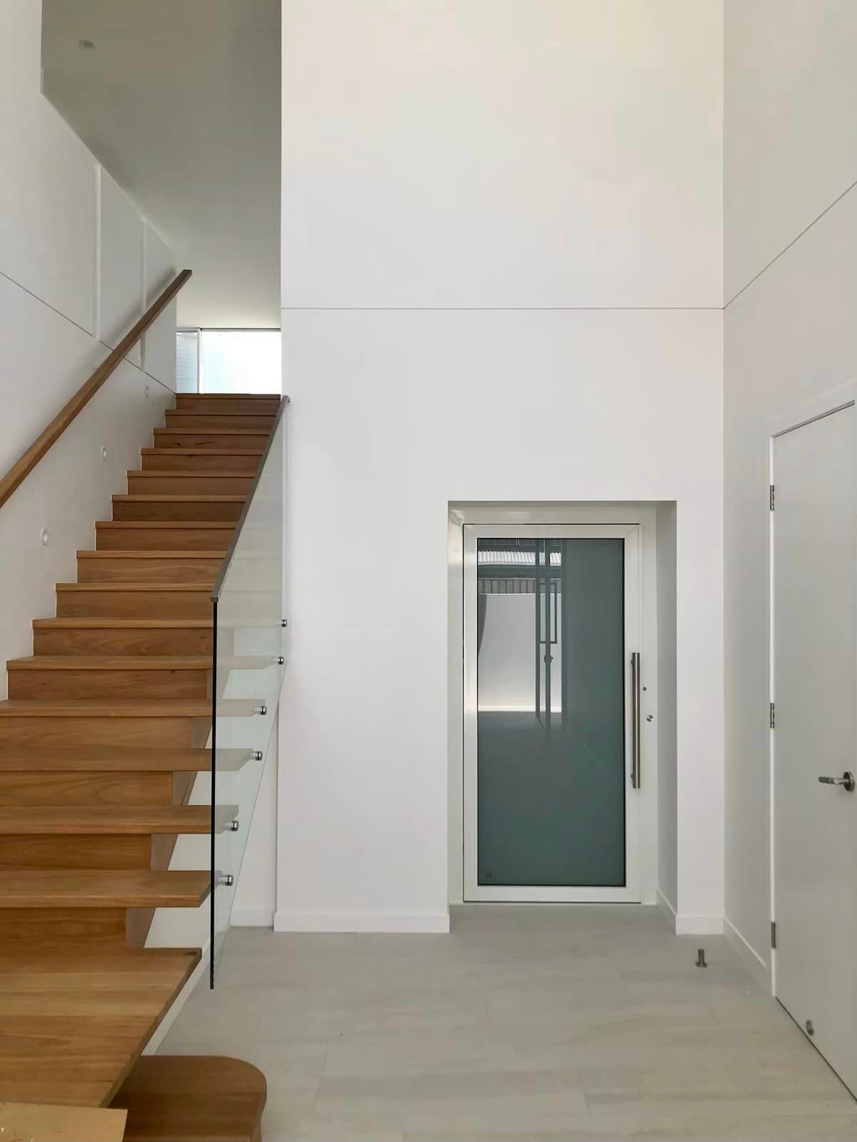 A Wooden Staircase with A Glass Railing and A Glass Door — Master Lifts Cairns in Cairns, QLD