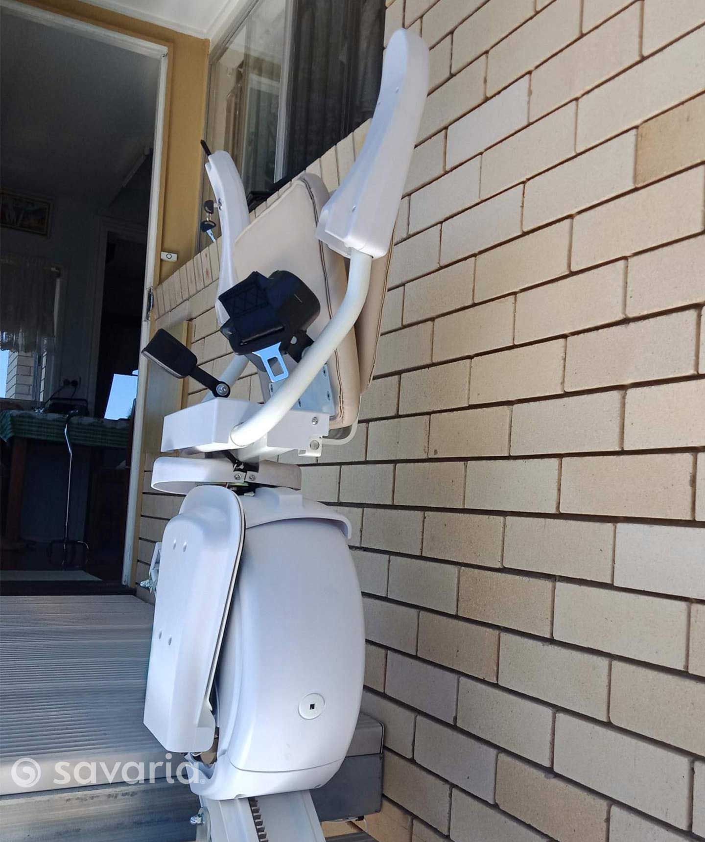 A White Stair Lift Is Attached to A Brick Wall — Master Lifts Cairns in Cairns, QLD