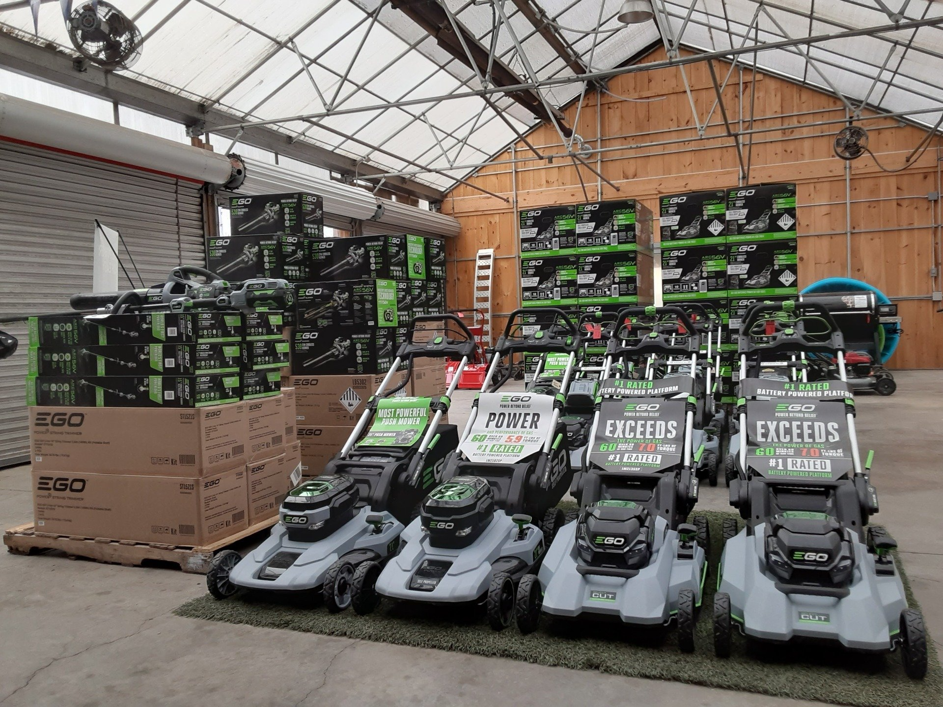 A display of EGO electric lawn mowers in a warehouse, with boxes stacked in the background.