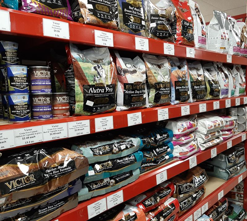 Shelves stocked with various bags of pet food, primarily dog food, in a store. Red shelves.