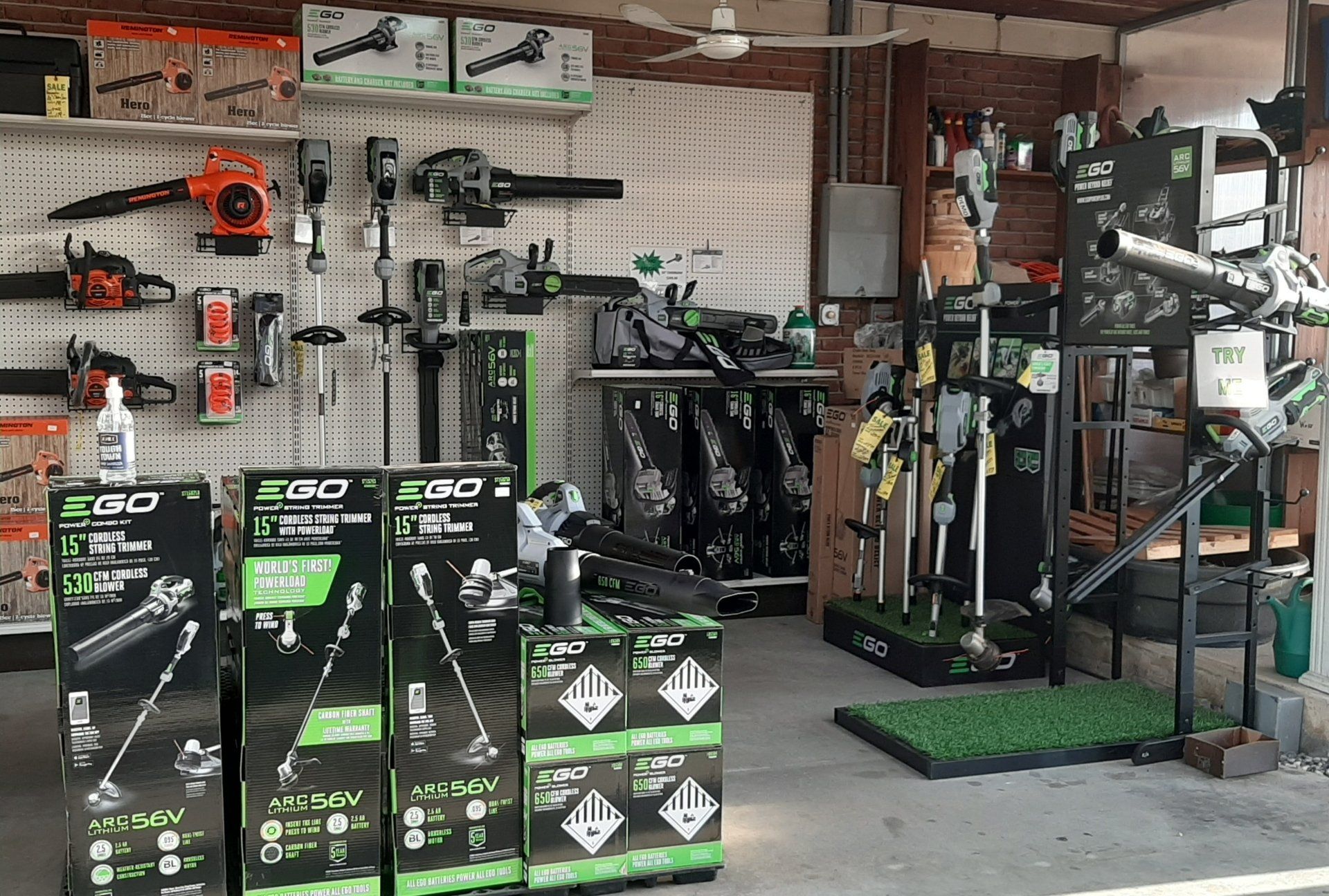 Lawn equipment store display with green and black battery-powered tools on shelves and stands.