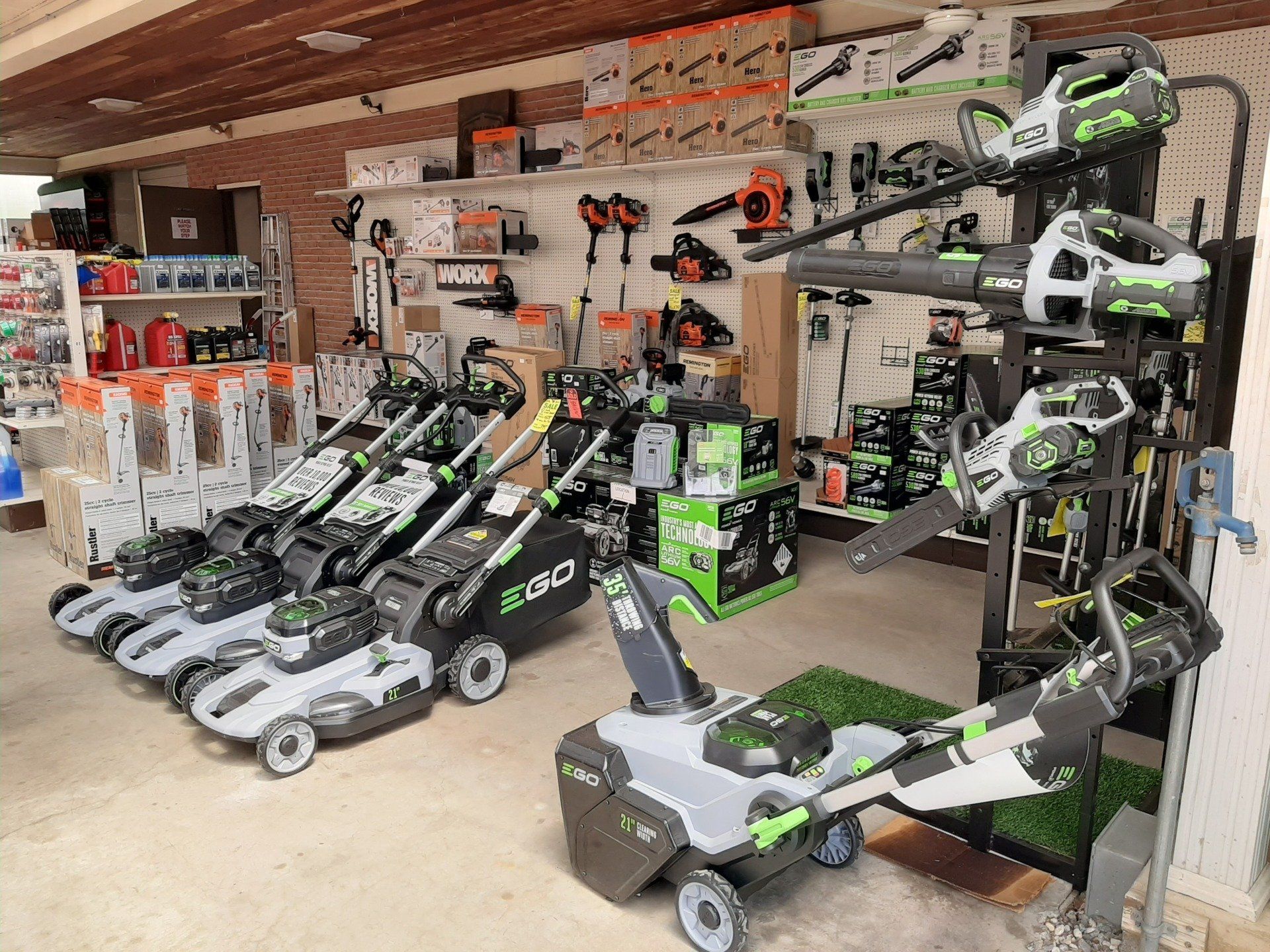 EGO lawn care equipment on display in a hardware store. Green, gray, and black tools. Mowers, blowers, and snowblower visible.