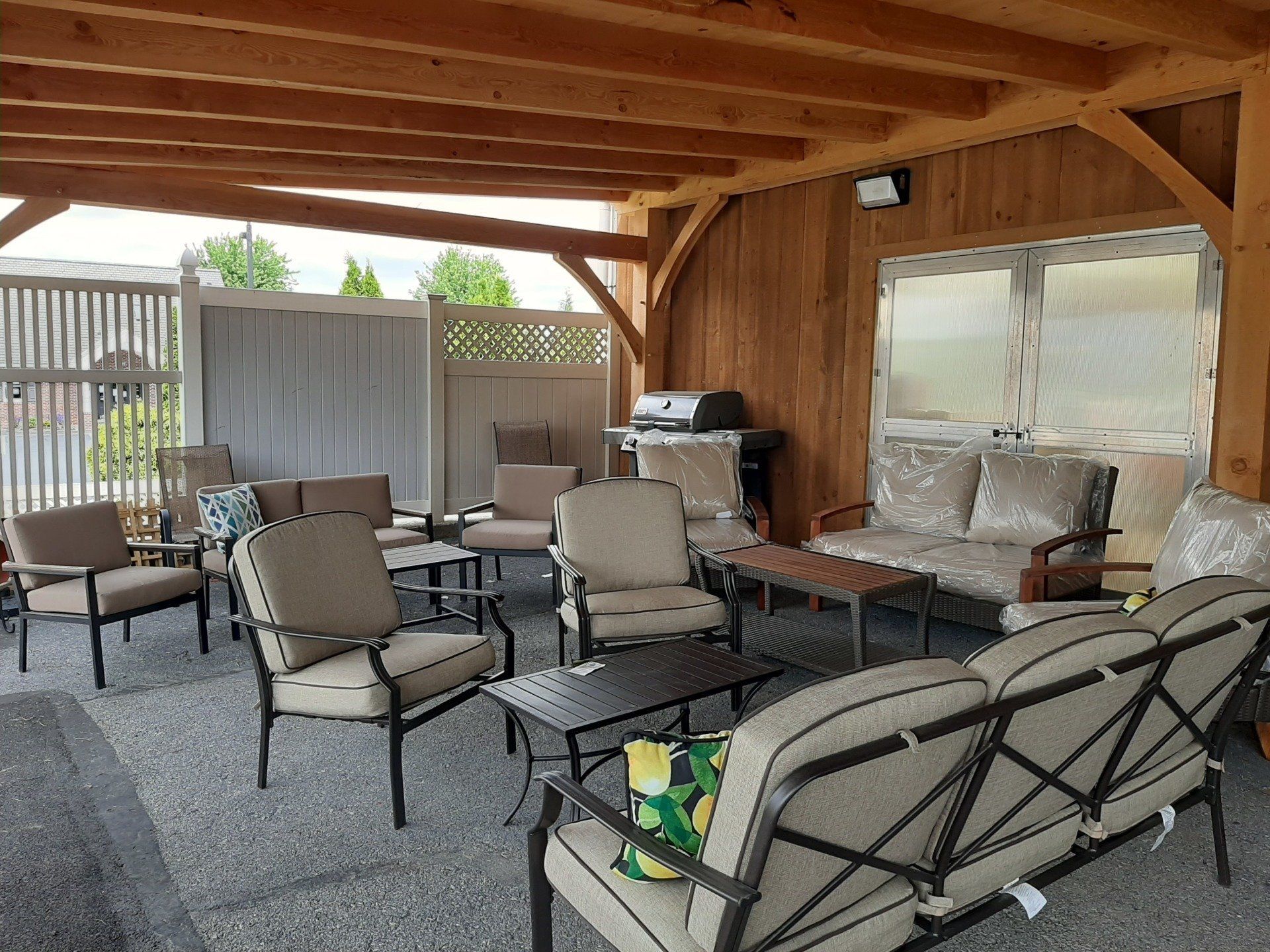 Patio with outdoor furniture: couches, chairs, tables, and a grill under a wooden roof.