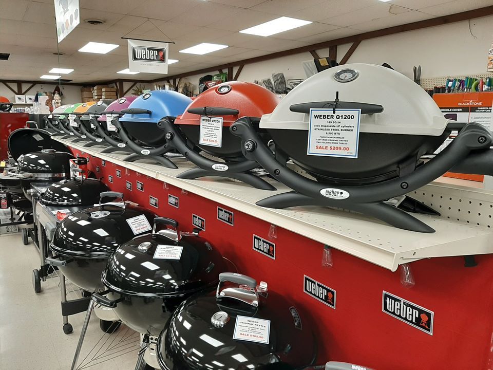 Row of colorful Weber grills on display in a store, including black, blue, red, and gray models.
