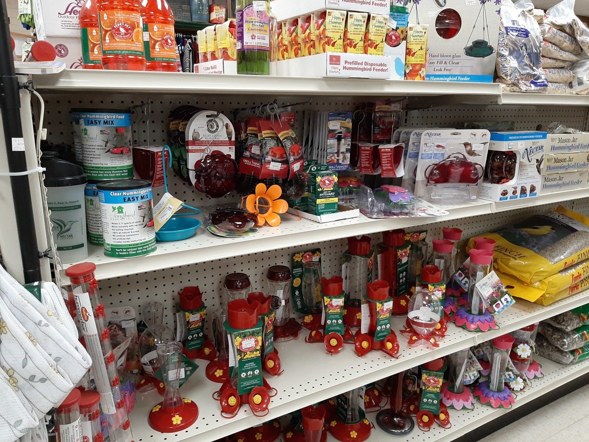 Shelves stocked with various red and green bird feeders and garden decorations in a store.