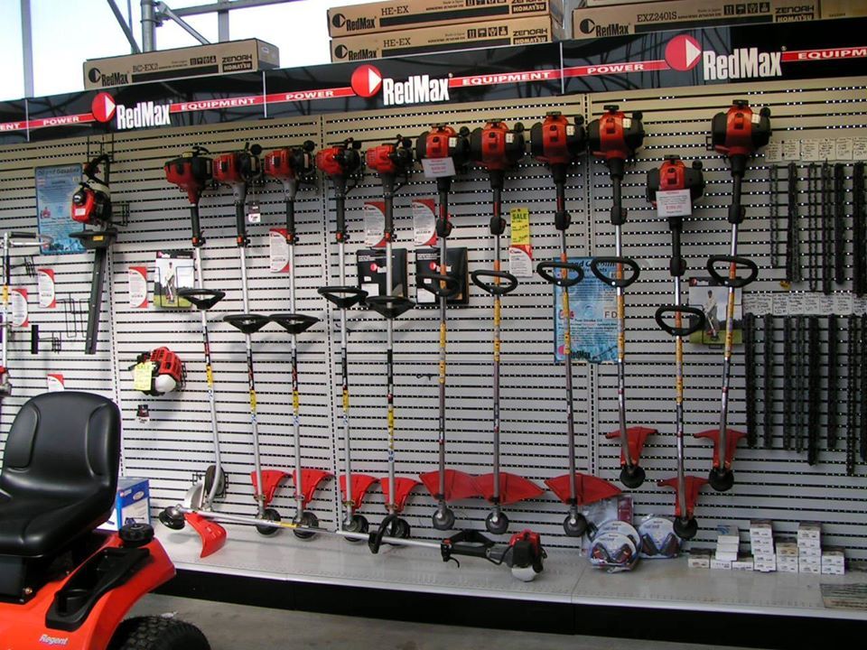 RedMax equipment display in store: String trimmers and leaf blower on wall, plus riding mower on the left.