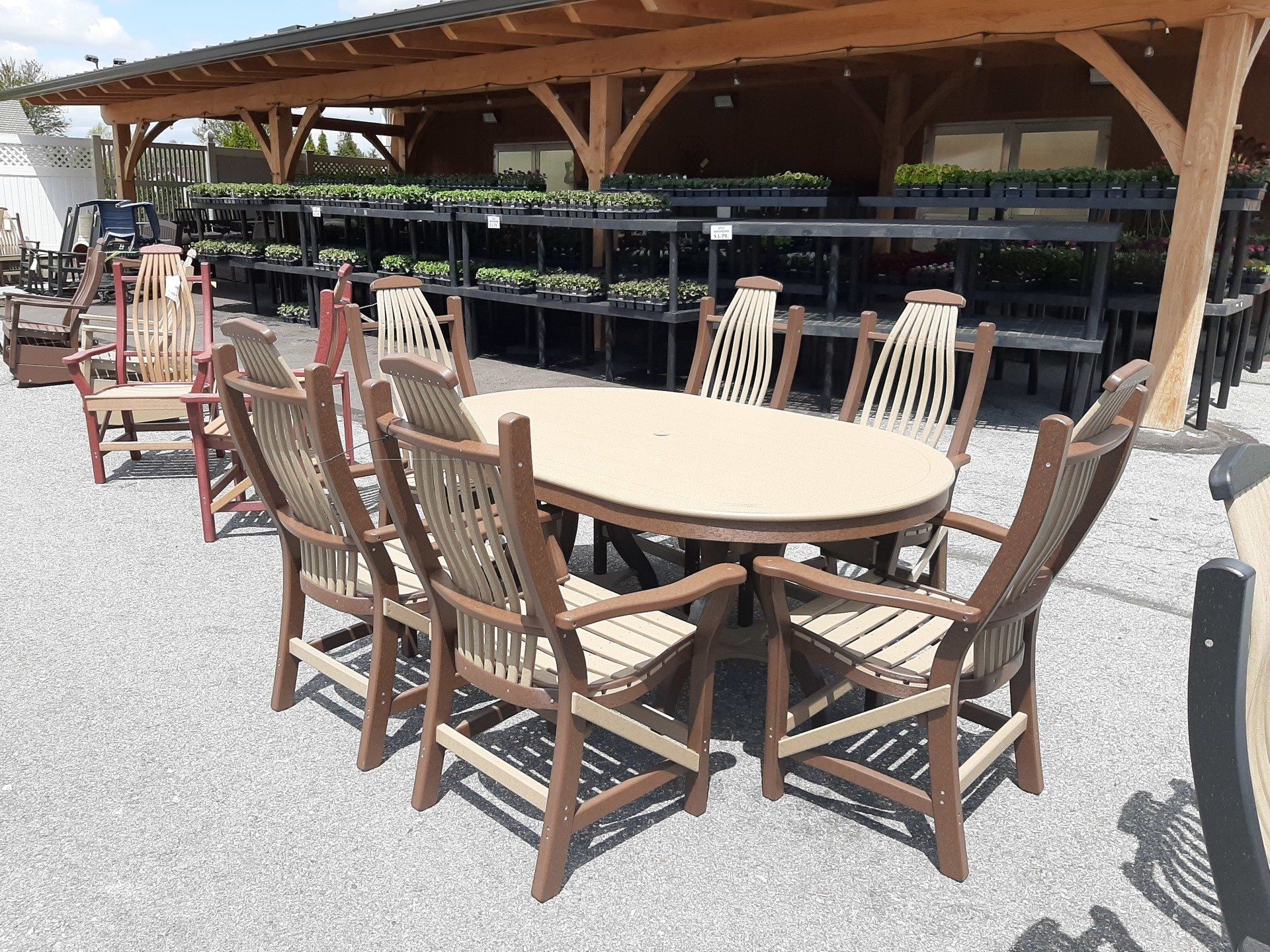 Outdoor dining set: oval table, eight brown and beige chairs, gravel ground, garden setting.