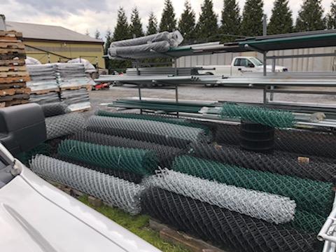 Rolls of chain-link fence in various colors at an outdoor supply yard.