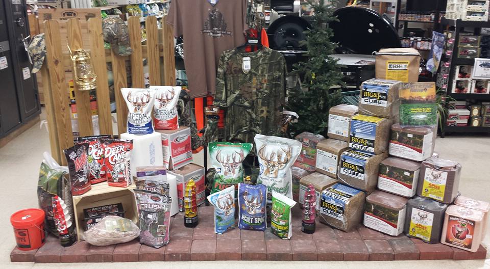 Display of hunting supplies, including feed, camouflage clothing, and a lantern, in a store setting.