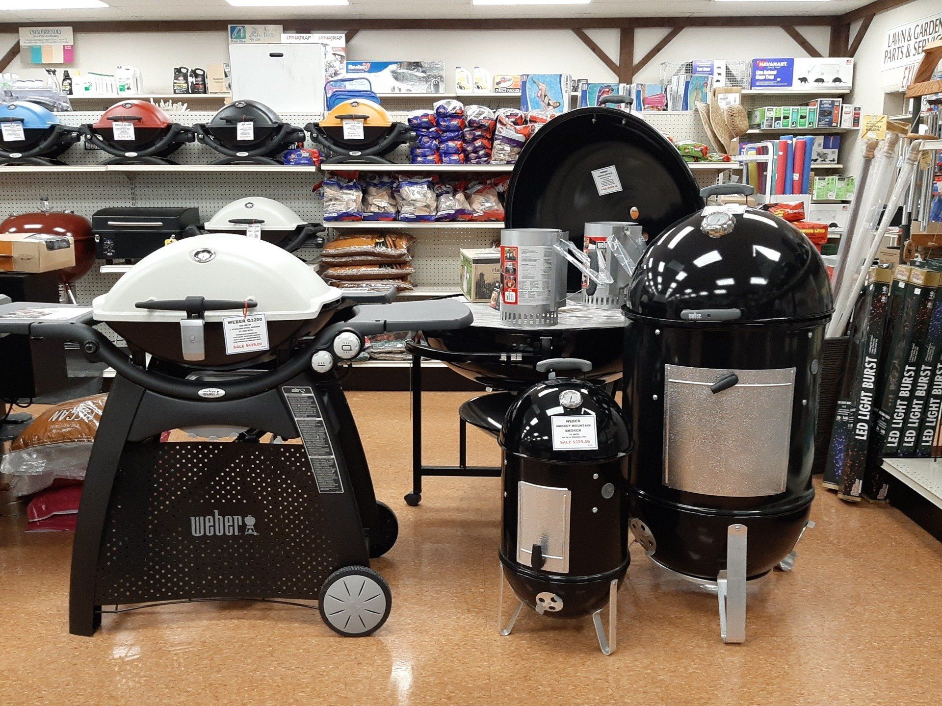 Grills for sale in a store; includes a gas grill, smokers, and other grilling supplies.