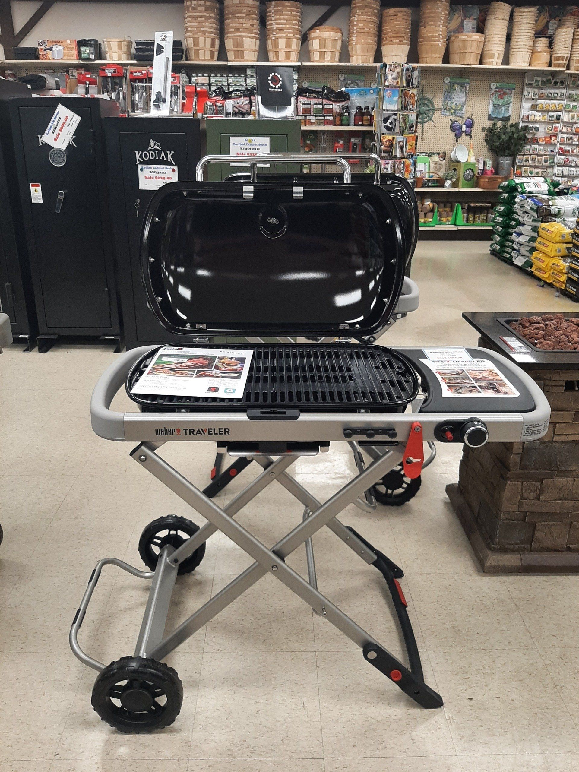 Gray and black portable gas grill with open lid and cart, inside a store.