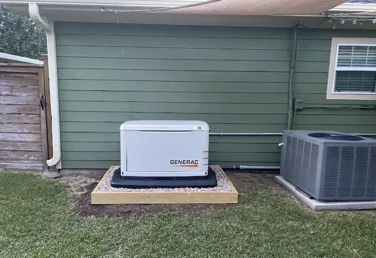 A generator is sitting in the backyard of a house next to an air conditioner.