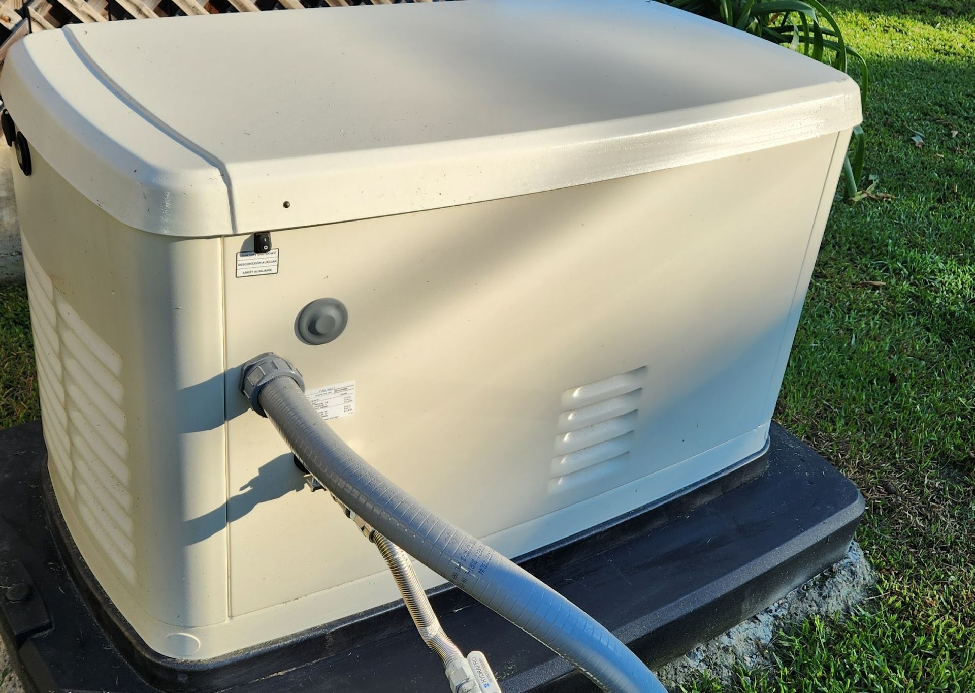 A white box with a hose attached to it is sitting in the grass.