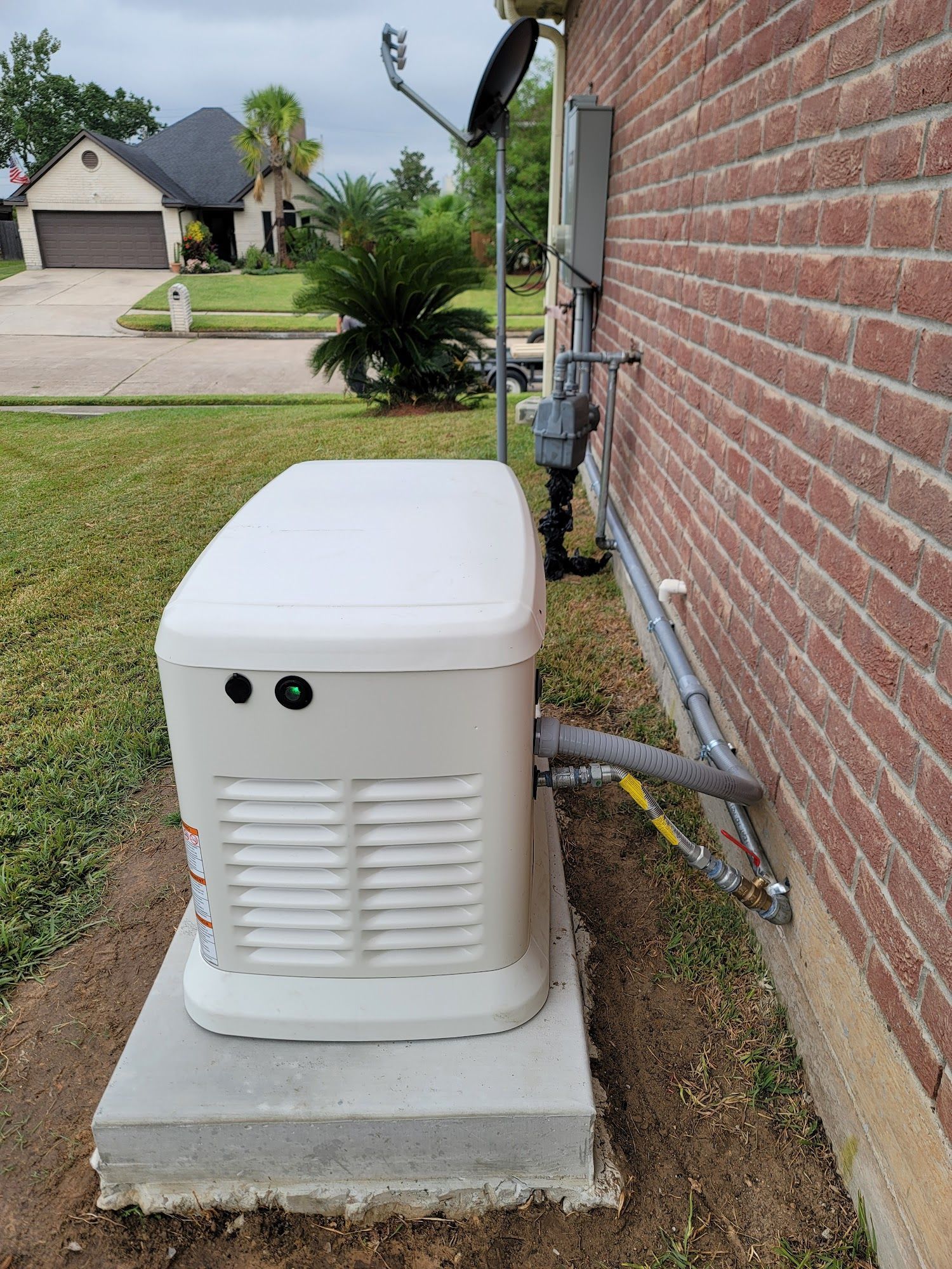 A white generator is sitting on the side of a brick building.